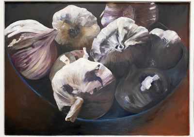 A monochromatic palette of off white, cream, light burgundy and dark blue greys. Garlics are placed in a bowl and are strongly lit, casting strong shadows. The garlic stems form vertical lines to contrast the round organic shapes.